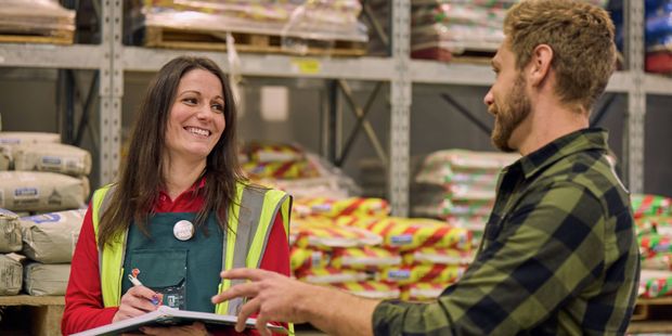Bunnings team member speaking with a customer in the timber yard of a Bunnings store stocked with building materials.