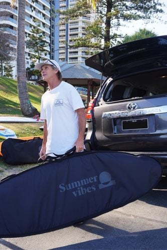 Man loading a large black Summer vibes surfboard travel bag into the back of a four wheel drive.