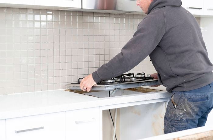 A person is disconnecting a gas cooktop carefully before any removal work begins.