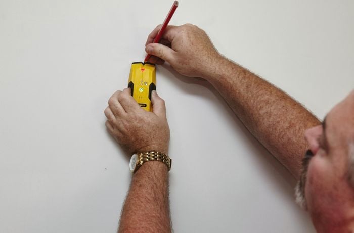 A person marking a wall using a stud finder