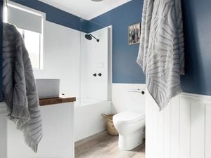 White modern bathroom with plush bath towels, toilet and shower over a bath.
