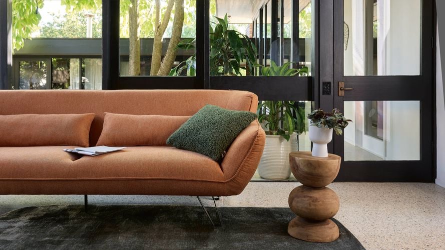 Burnt orange lounge, timber side table all sitting on a thick charcoal rug in living room.