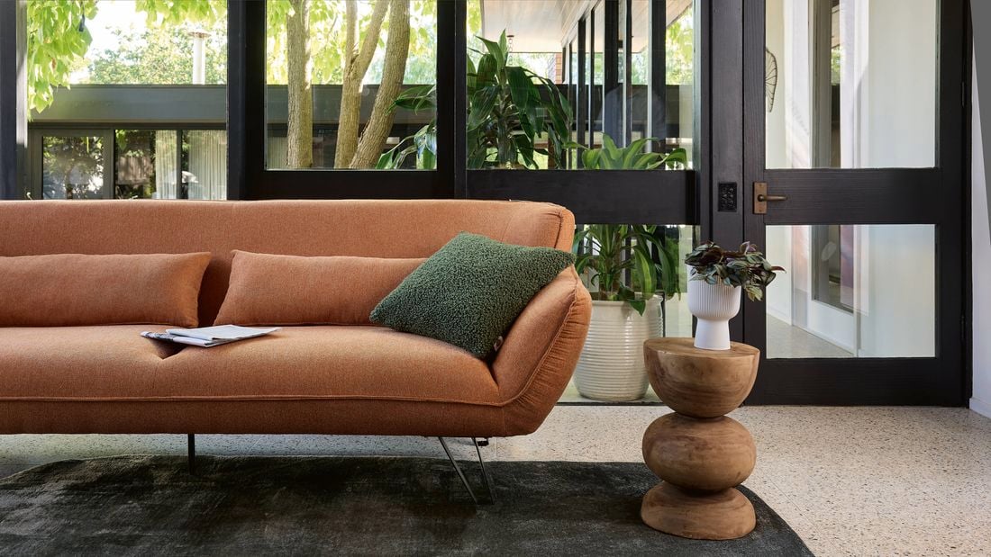 Burnt orange lounge, timber side table all sitting on a thick charcoal rug in living room.