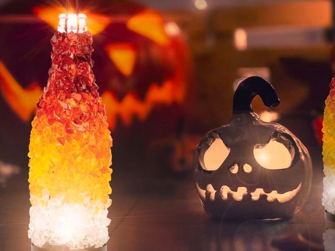 Mosaic lantern in orange, red and clear glass sitting next to a ceramic carved pumpkin candle holder. 