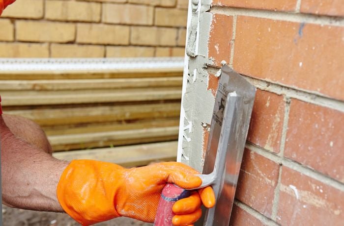 A person applying render over angle beading at the corner of a brick wall