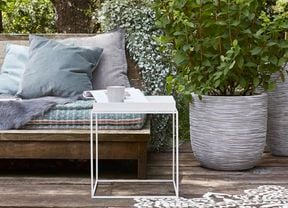 Outdoor setting with bench, cushions and lush green plants.