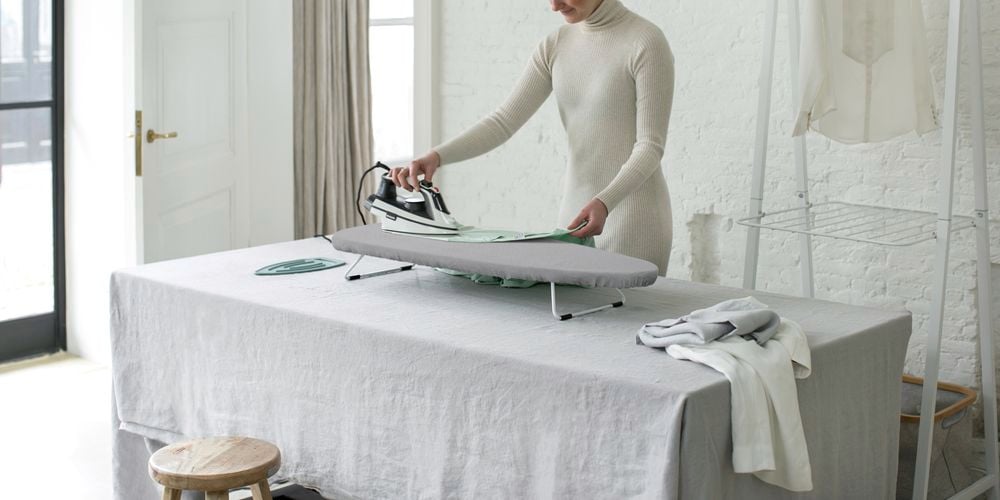 Lady using a table top ironing board set up in her living room