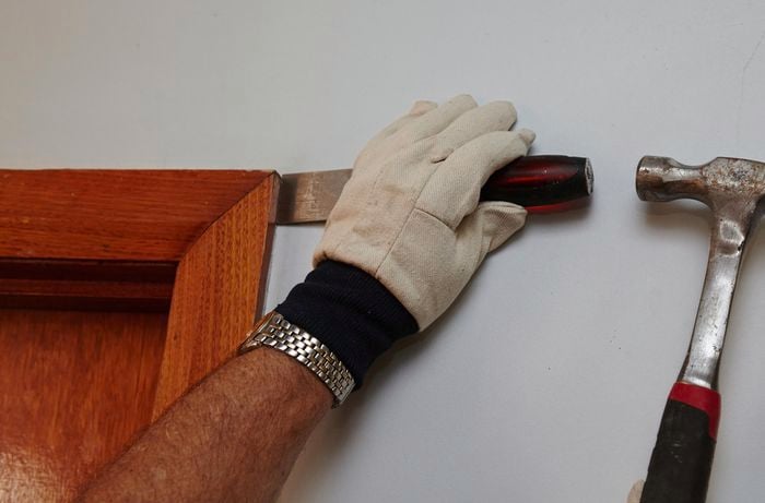 Person widening the gap between architrave and wall using a chisel and hammer.
