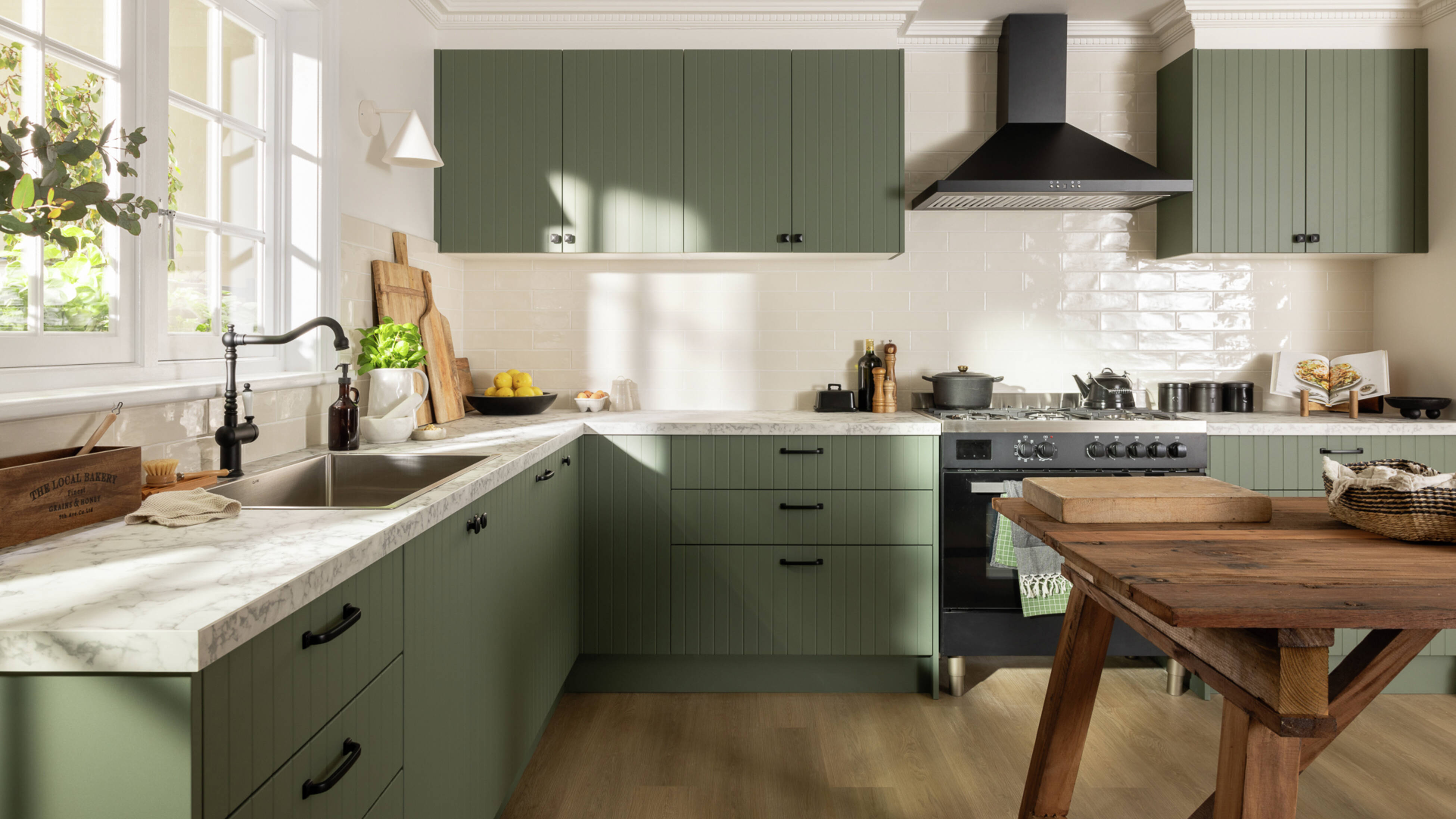 Green modern kitchen with a white marble benchtop, black sink mixer and a wooden table in it.