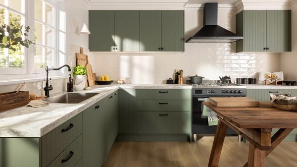Green modern kitchen with a white marble benchtop, black sink mixer and a wooden table in it.