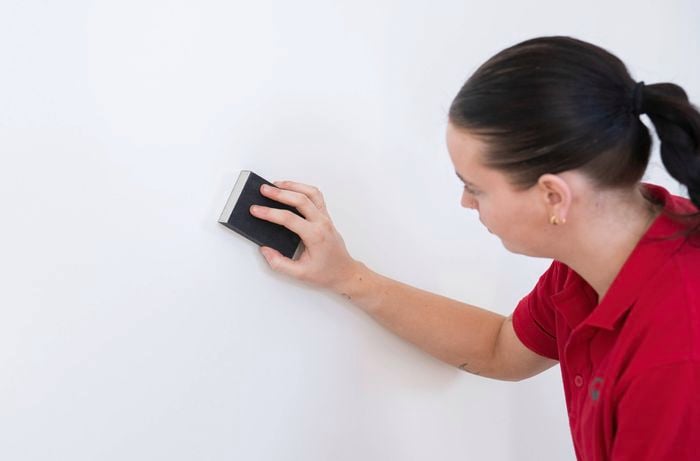Sand uneven areas to smooth over filler patches and even out imperfections   Image Description: A Bunnings Team Member is sanding a wall with a sanding block to smooth over filler patches and even out any imperfections.