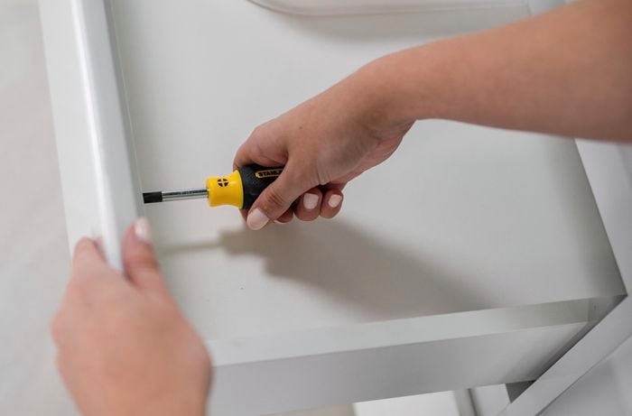 Pilot hole and screws being drilled into a vanity with a screwdriver