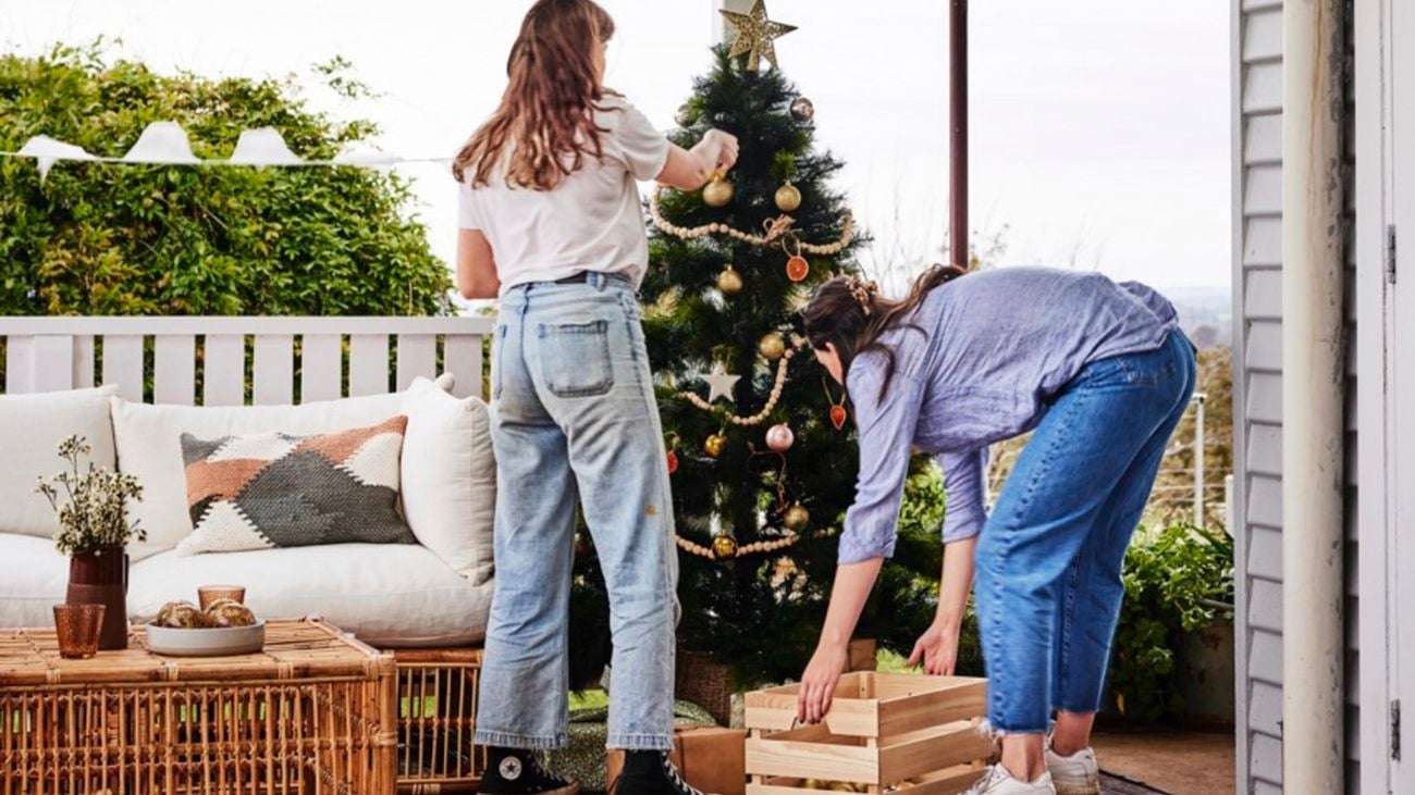Two people on a verandah, one holding a wooden storage crate, disassembling a christmas tree.