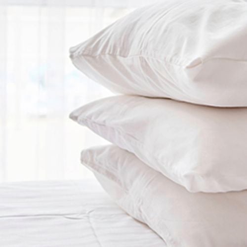 Three white pillows stacked neatly on a bed.