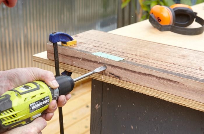 Person creating a hole in a bit of timber using a drill with spade bit.