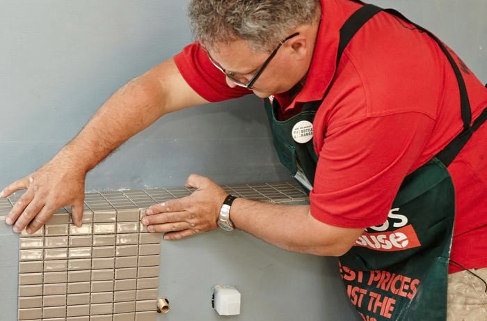 Mosaic tiles being held against a vertical feature wall by a Bunnings team member
