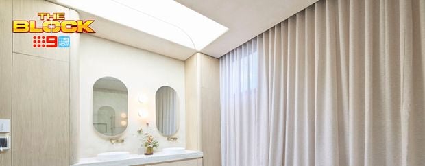 A modern bathroom with curtains, a bath, two mirrors on the wall, two sinks with drawers underneath and a wardrobe in it.