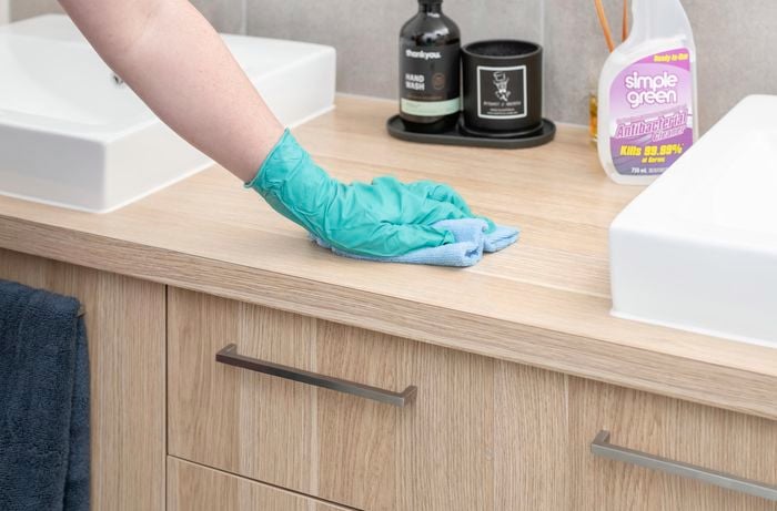 Person wearing a glove wiping bathroom sink benchtop with a cloth.