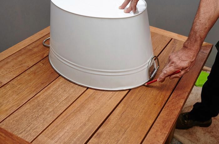 Person holding a bucket upside down on top of a table and a tracing around it with a pencil.