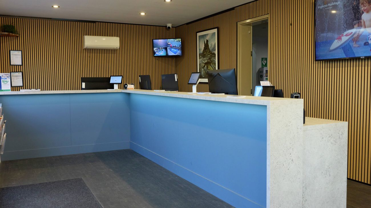Reception area with a modern blue service counter, timber feature walls, computer workstations and digital display screens.