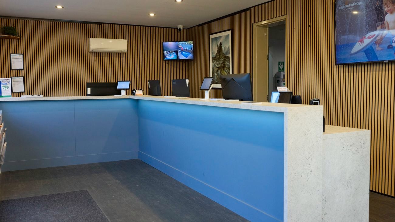 Reception area with a modern blue service counter, timber feature walls, computer workstations and digital display screens.