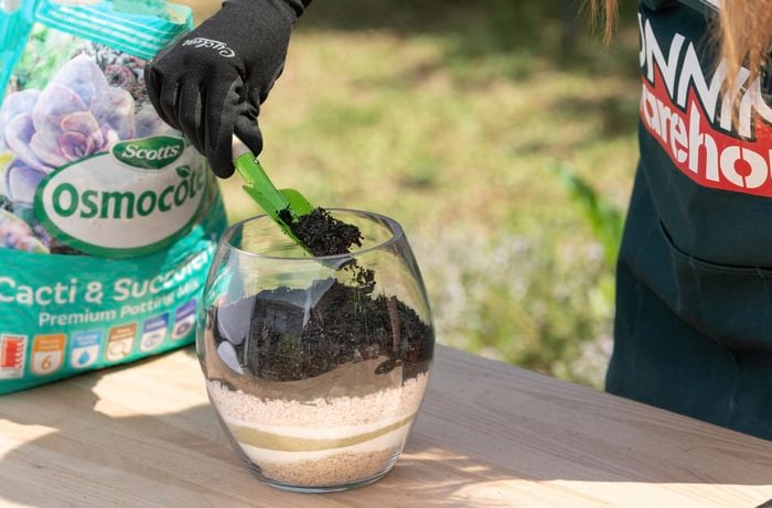 Person scooping potting mix into see-through stone pot.