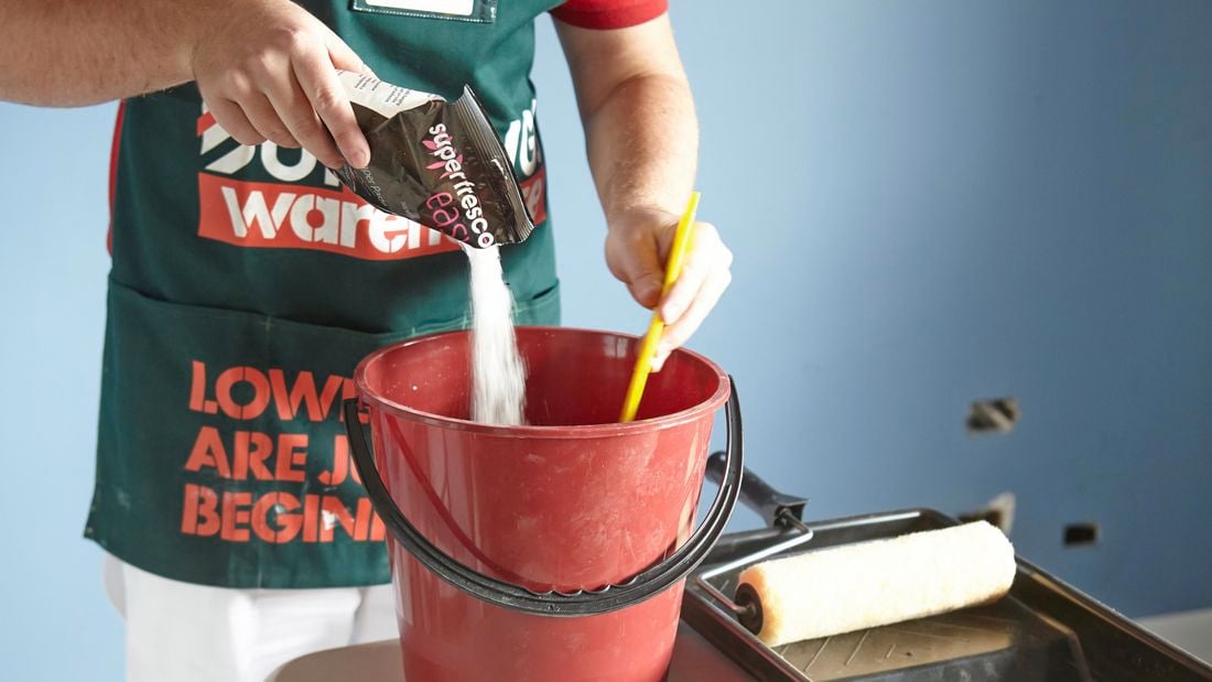 Bunnings team member pouring wallpapering solution into a bucket while stirring