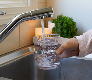 Person filling a glass with water from a kitchen mixer tap
