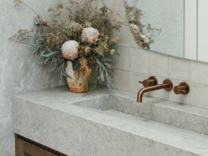 Bathroom vanity with stone surfaces, brushed brass fixtures, a large mirror, and a floral arrangement in a ceramic vase.
