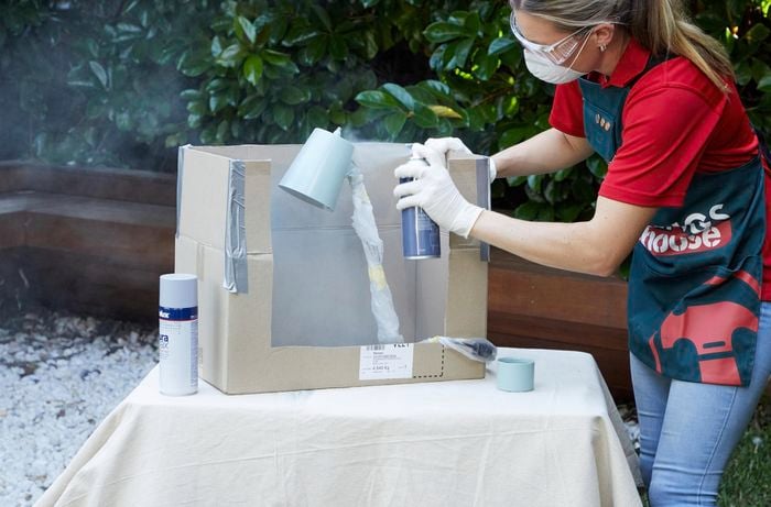 A woman wearing a Bunnings Warehouse apron spray paints a lamp using Dulux Duramax spray paint.