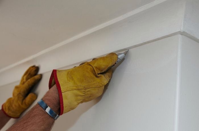A person cutting along the edge of a cornice with a trimming knife