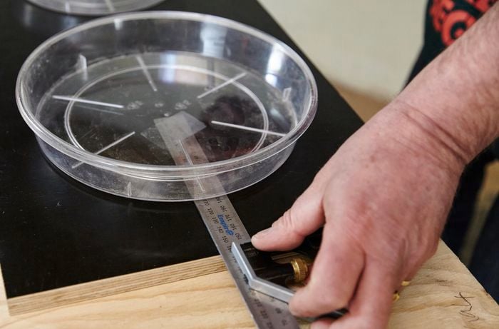 A person measuring the distance to the centre of a feeding bowl on a piece of plywood