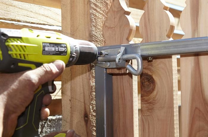 A person attaching a pad bolt to a metal gate frame using a cordless driver