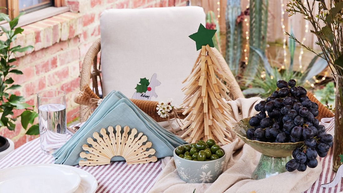 A table set with a clothes peg Christmas tree, a napkin holder made from clothes pegs, a kangaroo place holder, and bowls of grapes and olives.