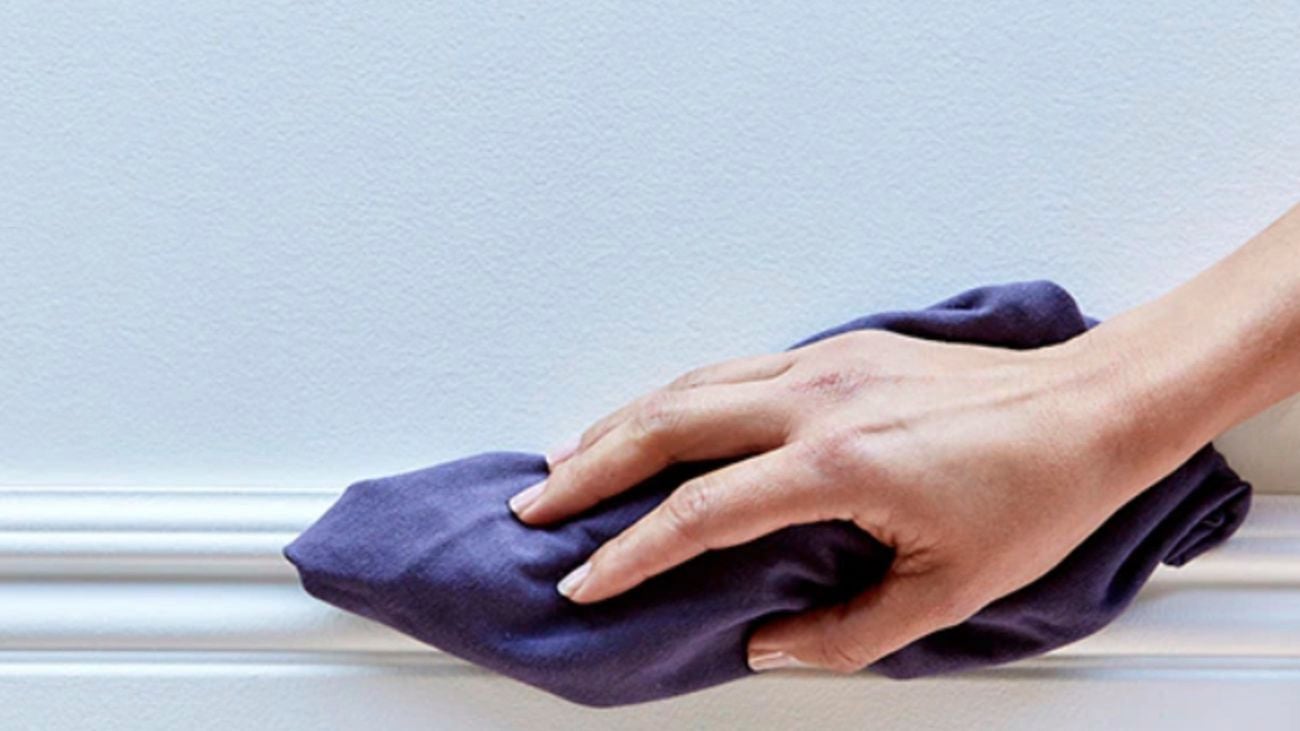 A hand wiping the top of a skirting board with a dry cloth