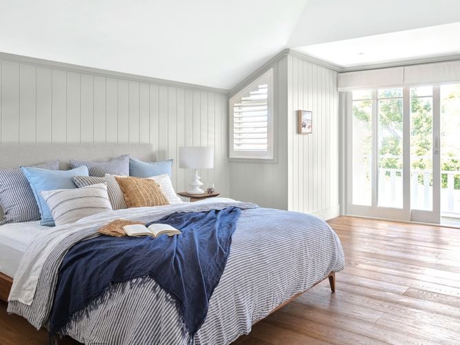 Bedroom with timber floorboards and low bed with pillows, blankets and cushions that opens out to a bright balcony