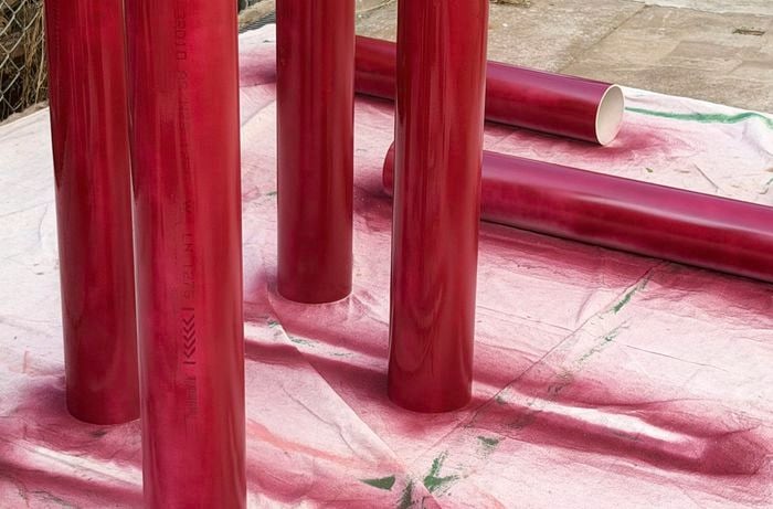 Red PVC pipes stand upright and lie flat on a drop sheet, freshly spray-painted.