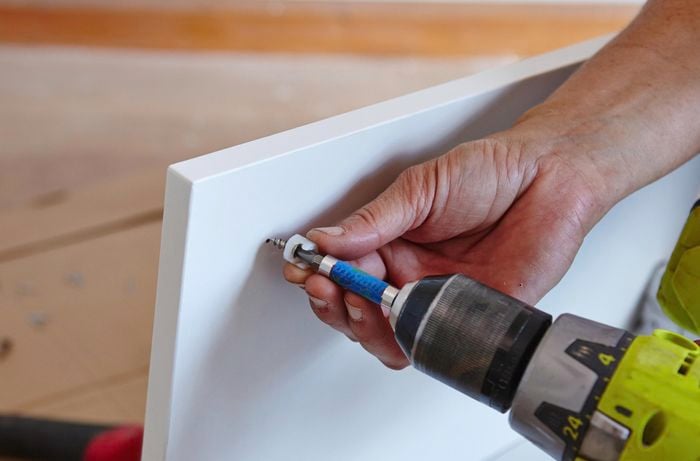 A person attaching a plastic bracket for a drawer rail using a cordless drill