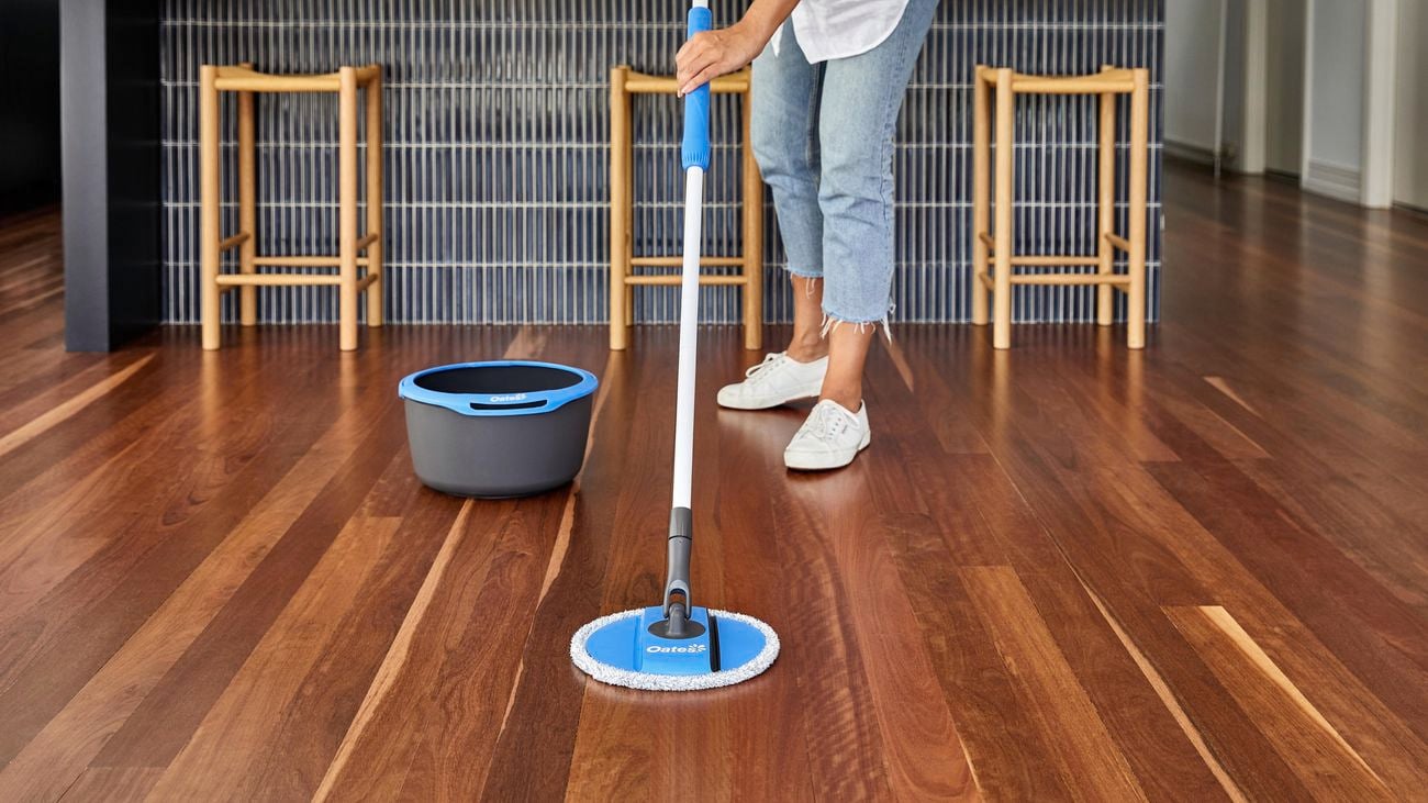 Person mopping hardwood floor with spin mop and bucket next to them.