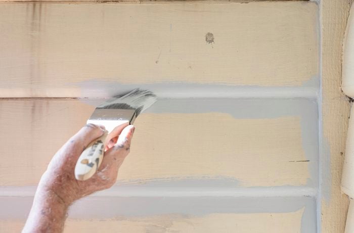 A person painting the edges of weatherboards