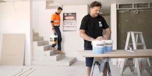 A tradie opening tubs of Gyprock adhesive on a work site.