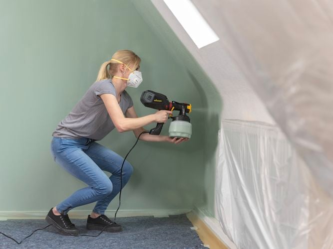 Wagner Flexio W575 with i-Spray attachment spraying olive green paint to a curved wall inside a home.
