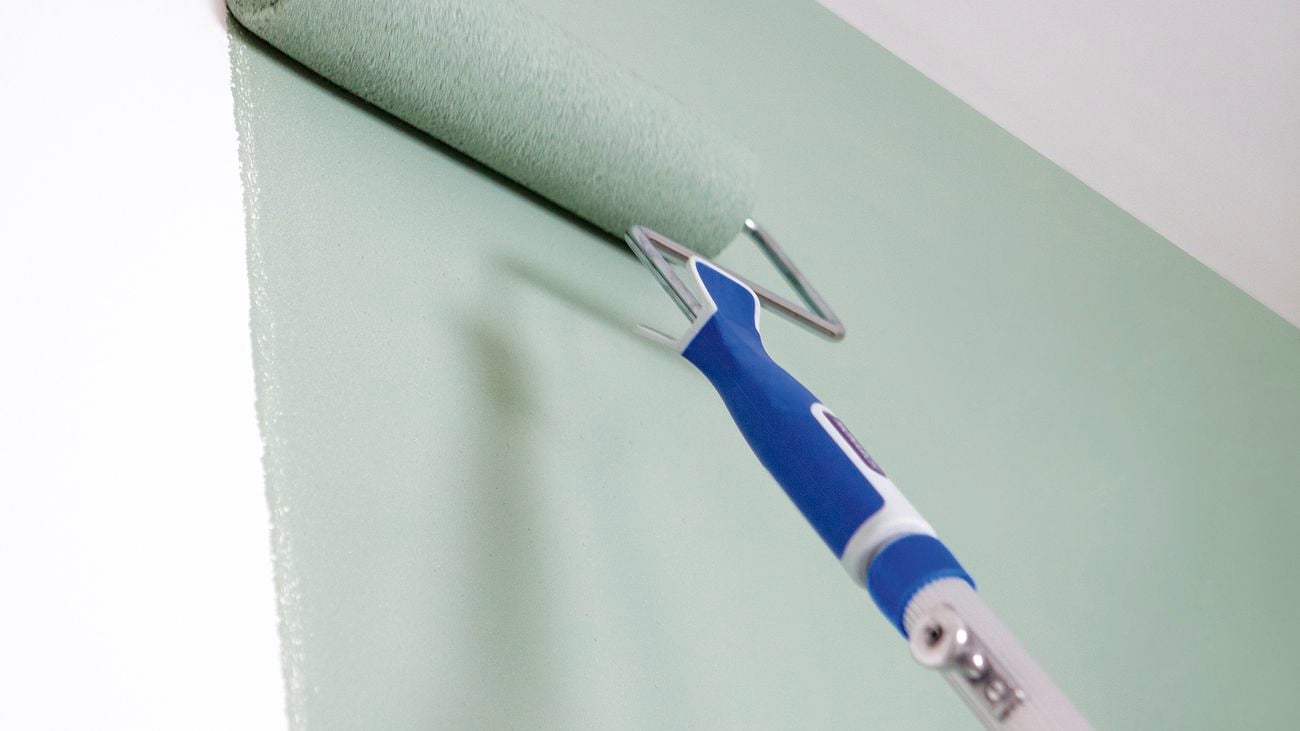 Microfibre paint roller painting a white wall with sage green paint