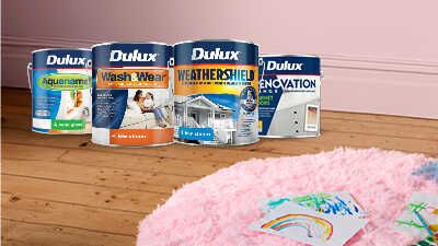 Four Dulux paint cans sitting on wooden floorboards in a pink room with a pink rug in the foreground