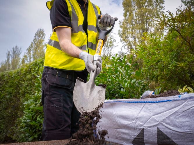 Person using a Roughneck Micro Round Shovel to move soil from a bulk bag.