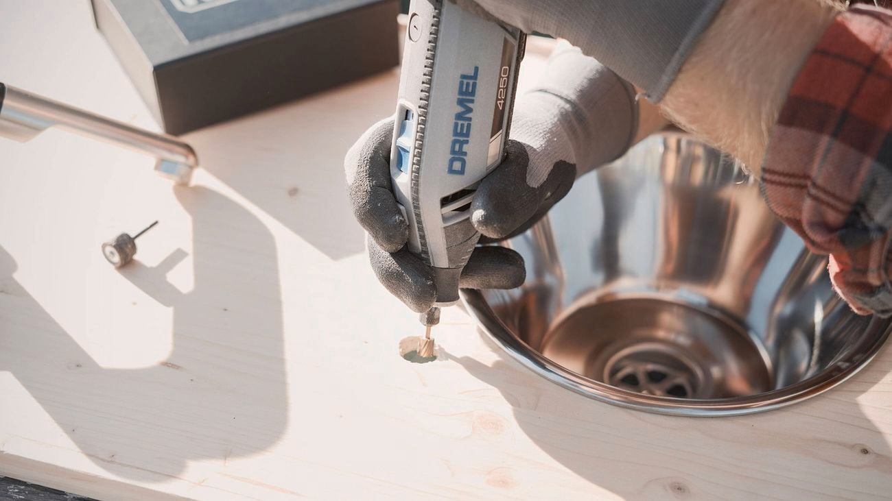 Man’s hands wearing gloves using the Dremel 4250 rotary tool to cut a hole in wood