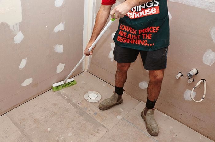 A person sweeping an untiled bathroom floor