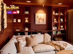 A cozy living room with a sectional sofa decorated with pillows and a blanket. Behind the sofa, built-in shelves display books, artwork, and decorative items, with a prominent horse painting at the center. The room features warm lighting and earthy tones, creating a welcoming ambiance.