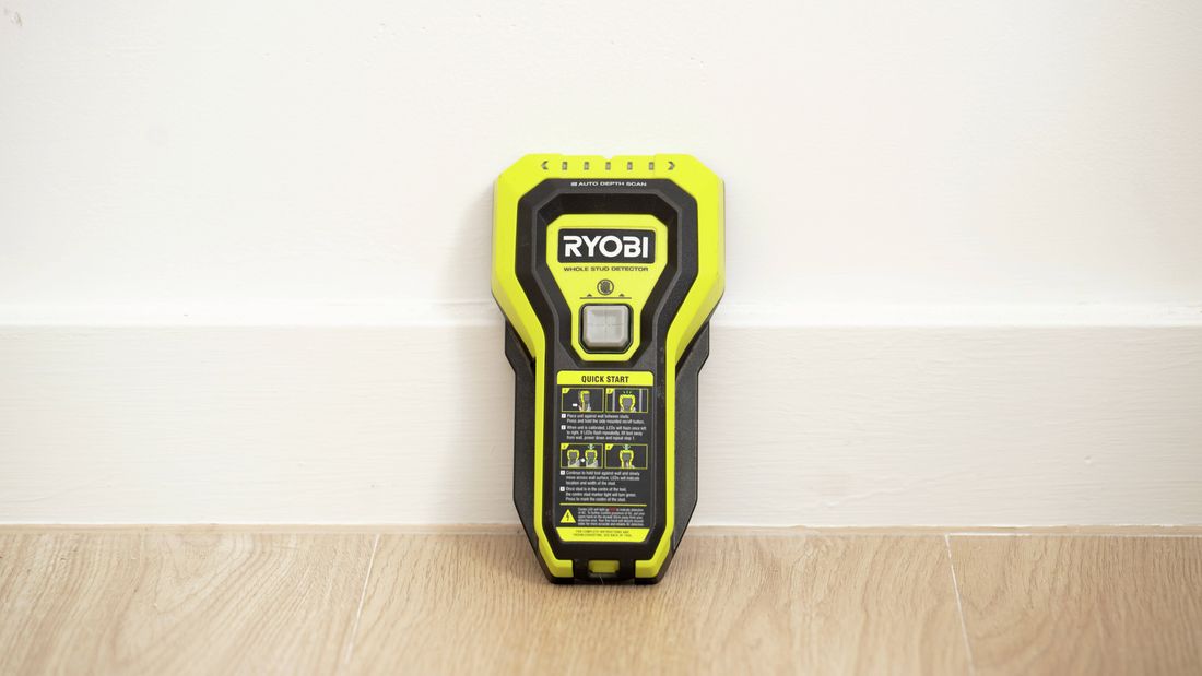 Yellow handheld stud finder standing upright against a wall.