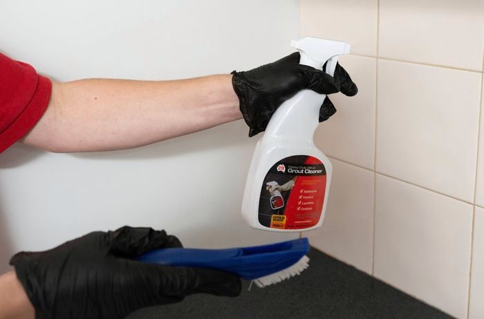 A person is holding a grout cleaner and brush for grout cleaning.